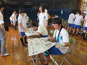 高齢者体験で白内障のゴーグルをつけて新聞を読む生徒の写真